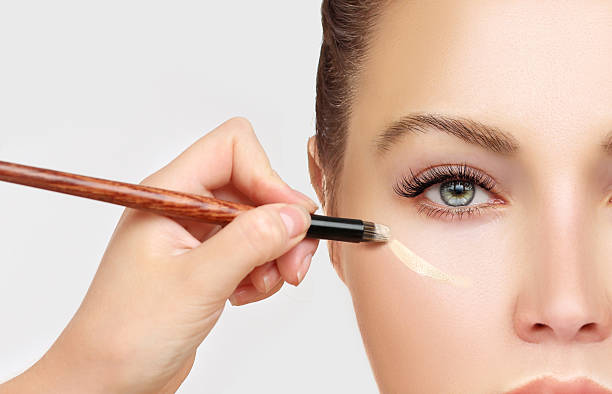 Ένα άτομο που χρησιμοποιεί ένα πινέλο Highlighter κάτω από τα μάτια του, δείχνοντας ένα κοντινό πλάνο του προσώπου του.